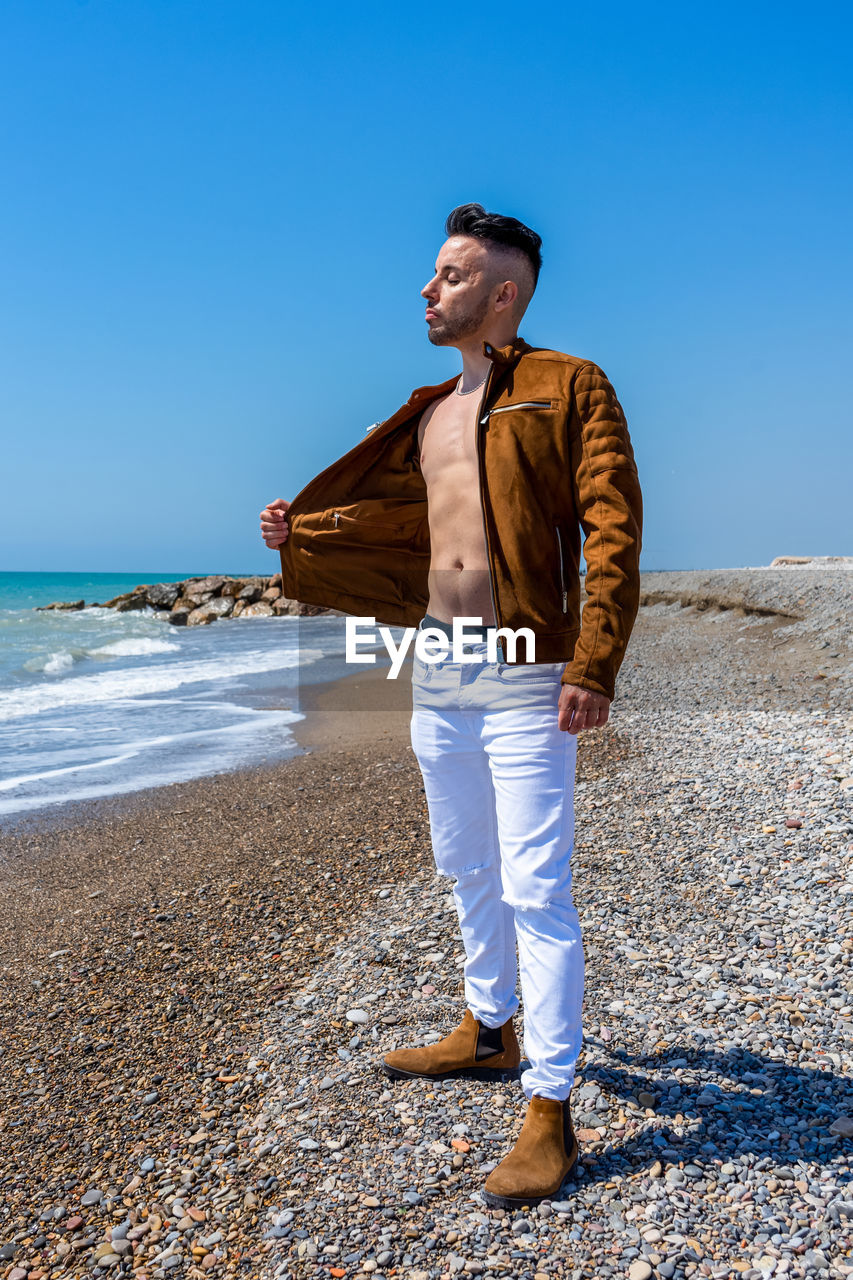 MAN STANDING ON BEACH AGAINST CLEAR SKY