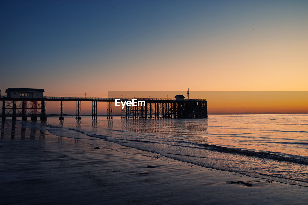 Pier on sea against clear sky during sunset