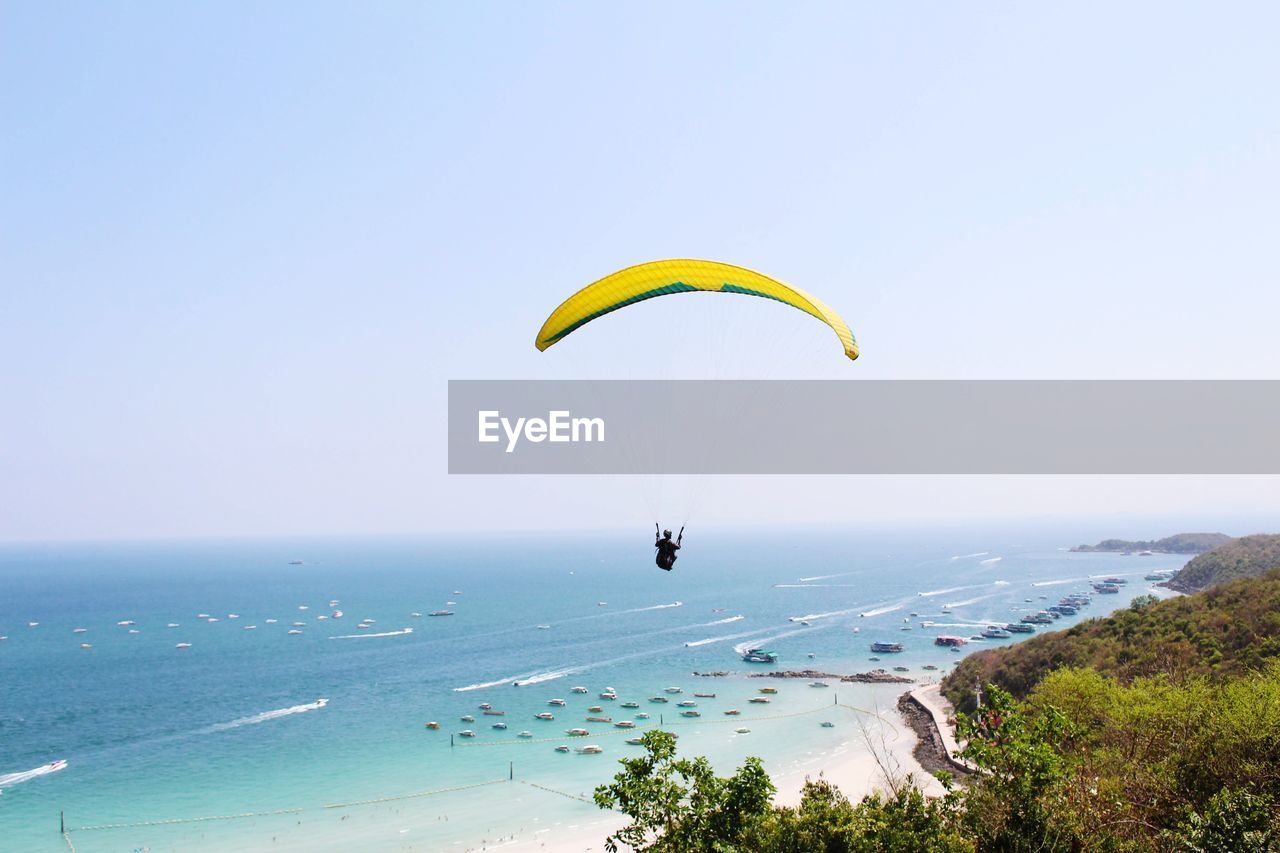 Person paragliding over sea against sky