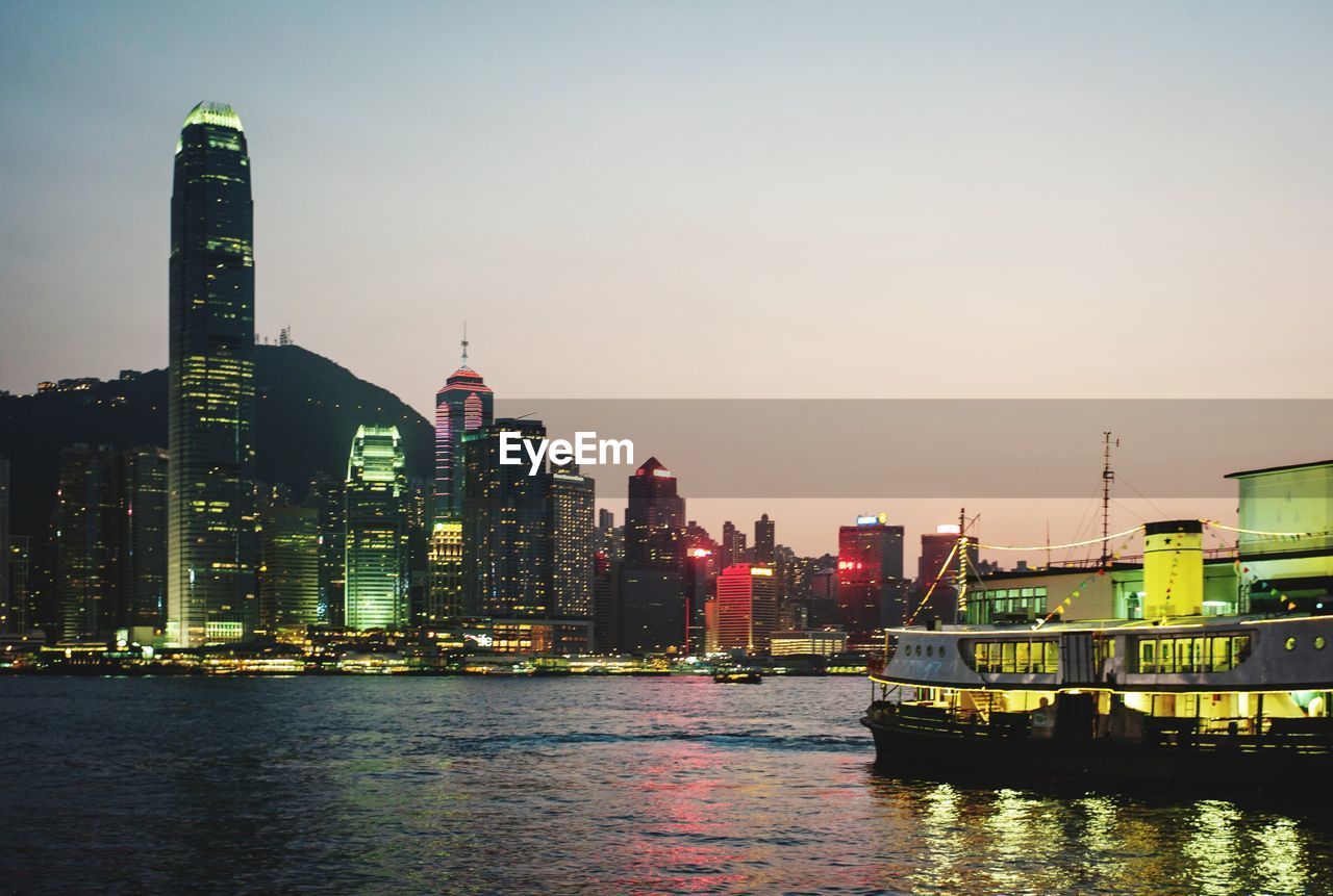 Illuminated buildings by river against sky in city