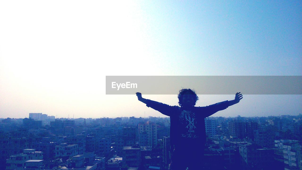 SILHOUETTE OF MAN WITH ARMS RAISED AGAINST SKY