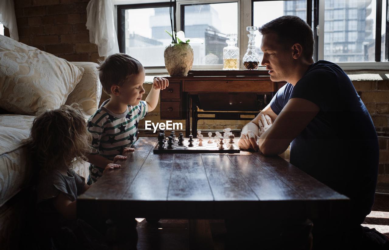 Father playing chess with children on table at home