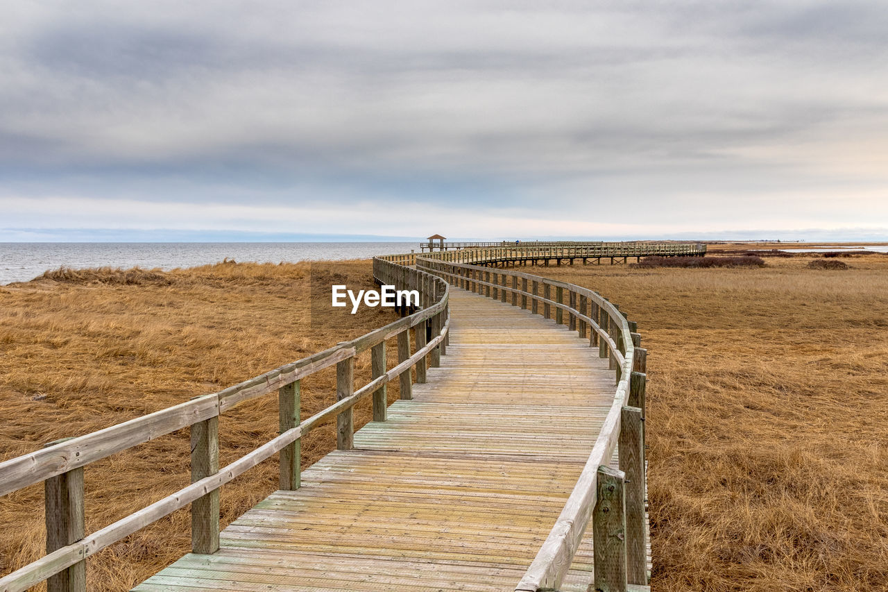 View of wooden footbridge leading towards sea against sky