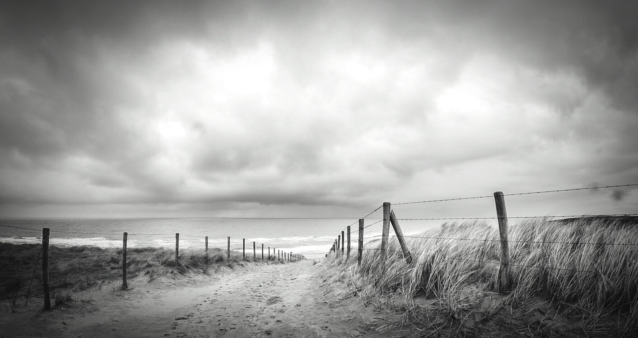 Pathway leading towards sea against cloudy sky