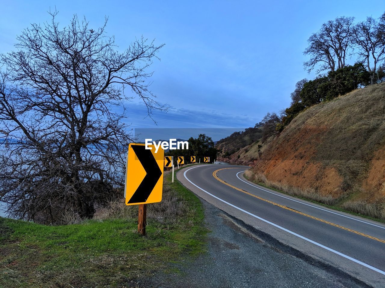 Directional road signs for curve on mountain highway. lake water in background.