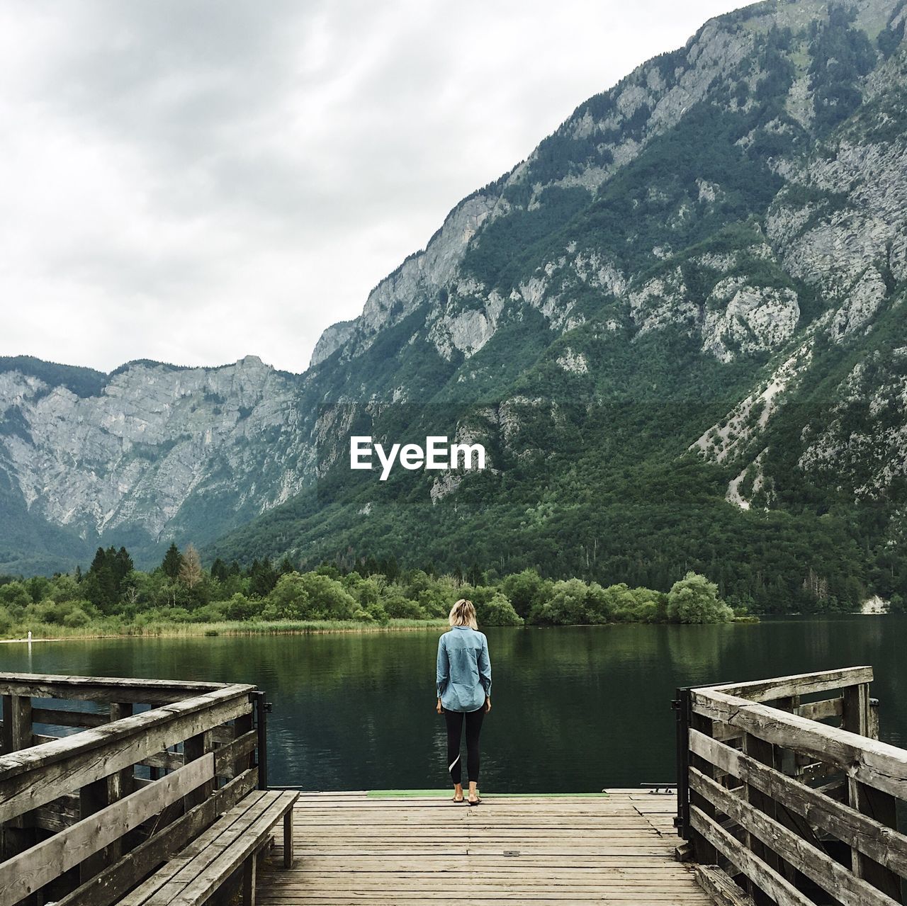 Rear view of man standing on pier over lake against mountain