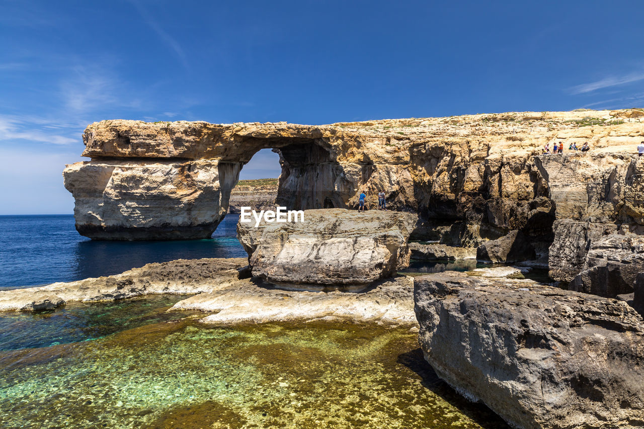 Rock formations by sea against blue sky