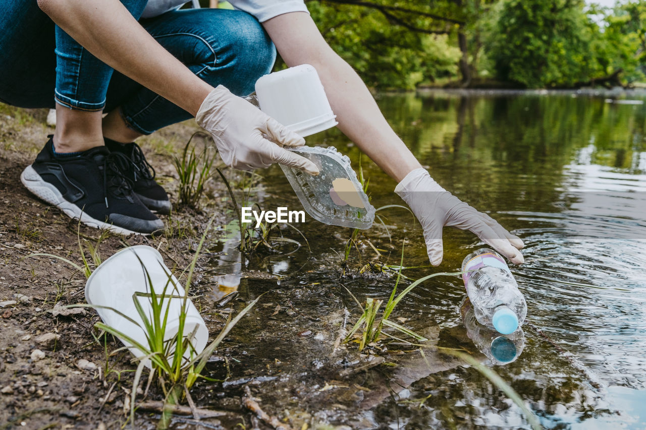 Low section of female volunteer cleaning plastic waste from pond at park