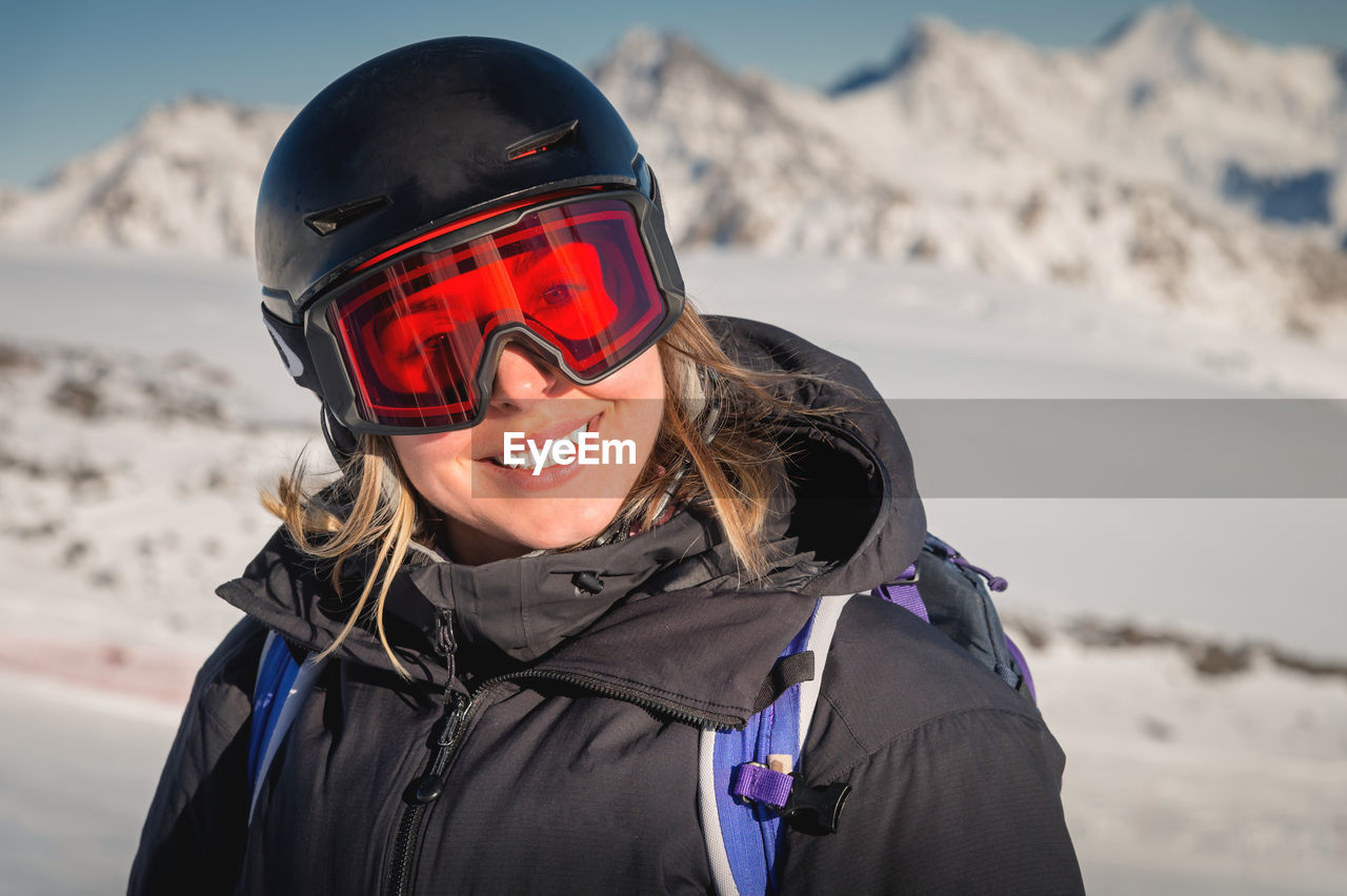Skier smiles in a safety ski helmet and goggles against the backdrop of the picturesque alpine