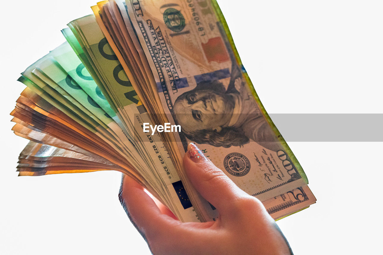 cropped hand of person holding paper currency against white background