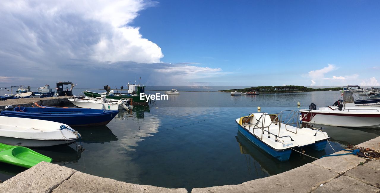 Boats moored at harbor against blue sky