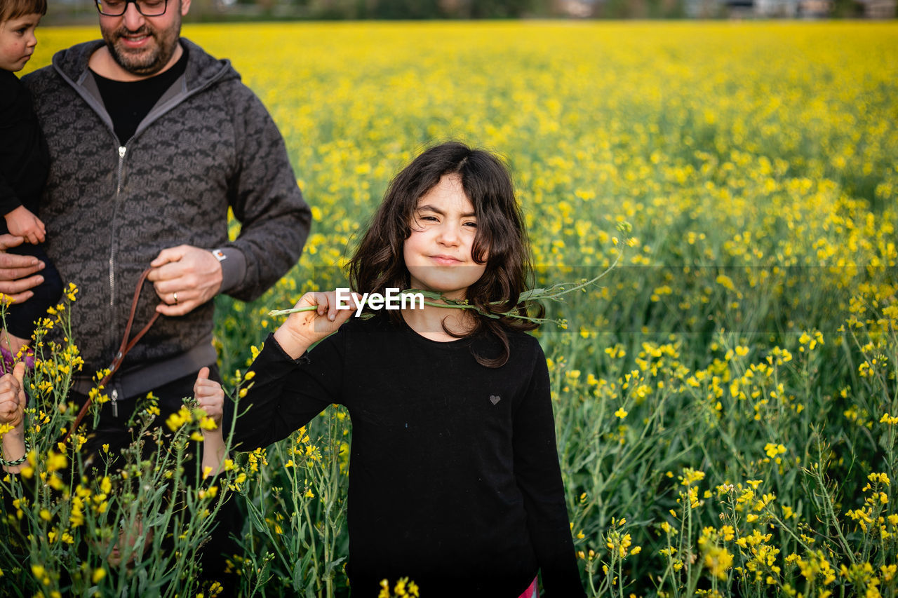 Portrait of a smiling girl standing in front of her father with other siblings amidst yellow flowers