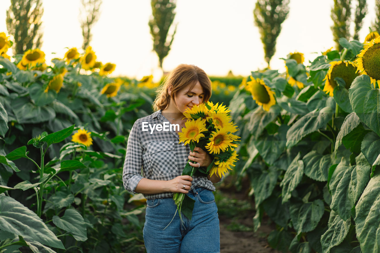 Beautiful young woman with sunflowers enjoying nature and laughing on summer sunflower field.