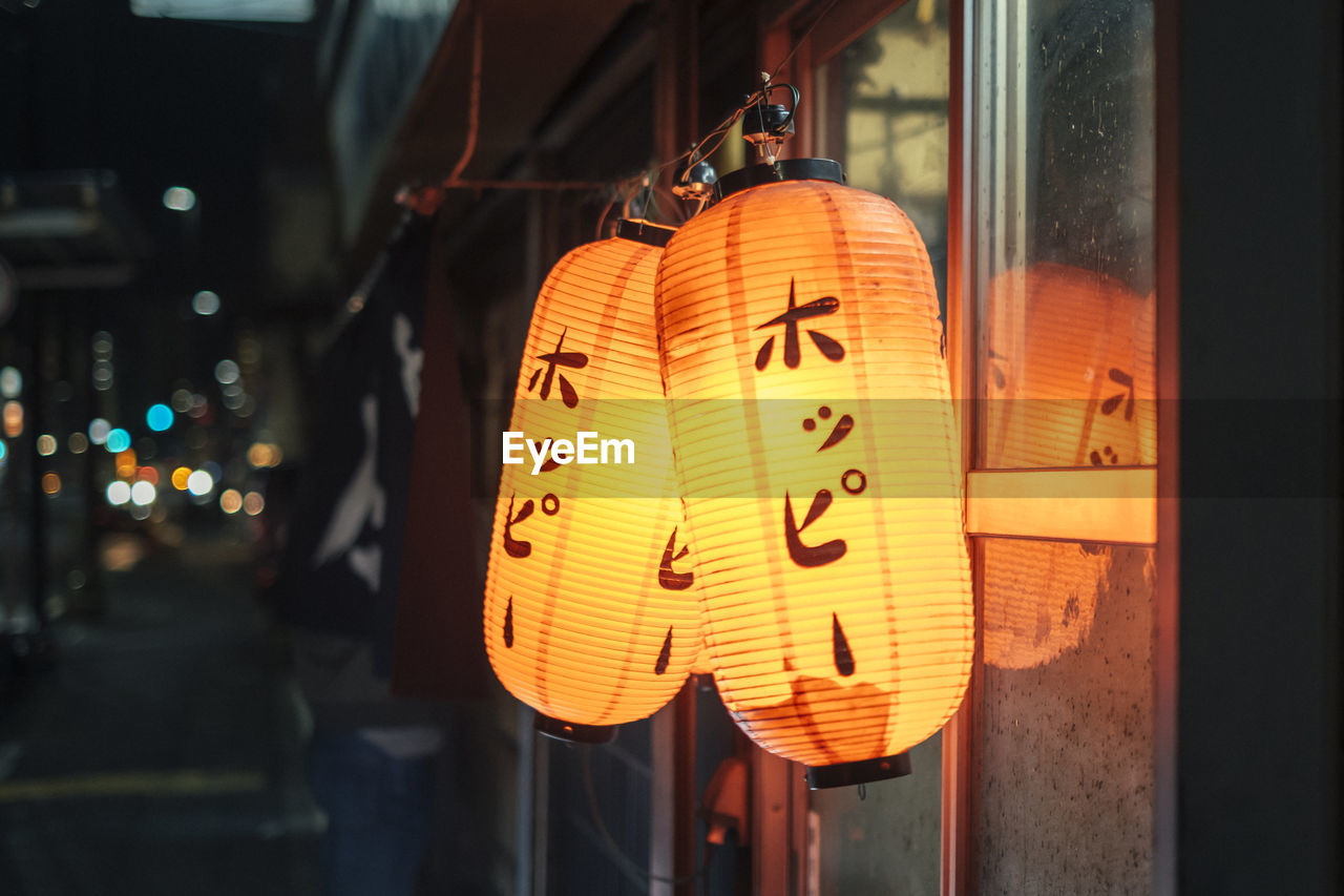 CLOSE-UP OF ILLUMINATED LANTERNS HANGING ON WINDOW