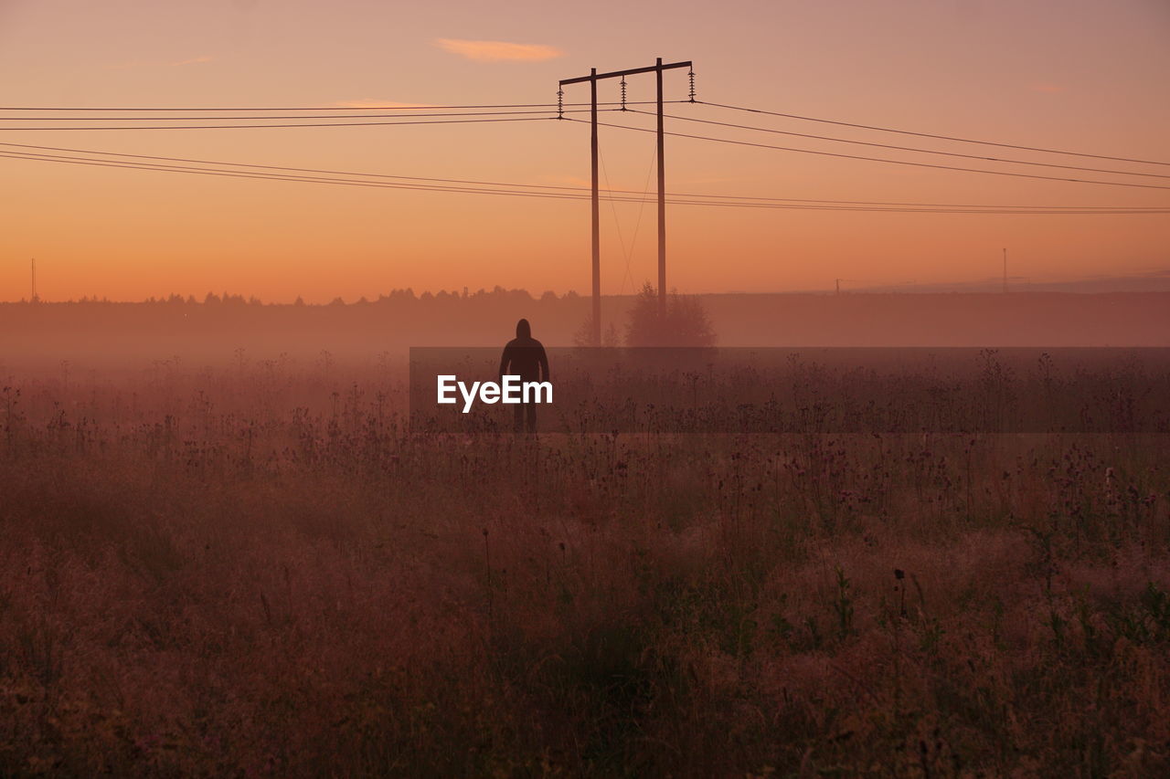 Man standing on field against sky during sunset