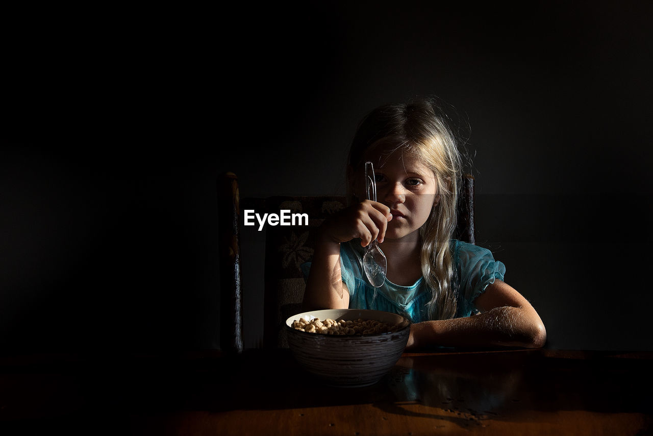 Little girl eating cereal in dramatic light looking at camera