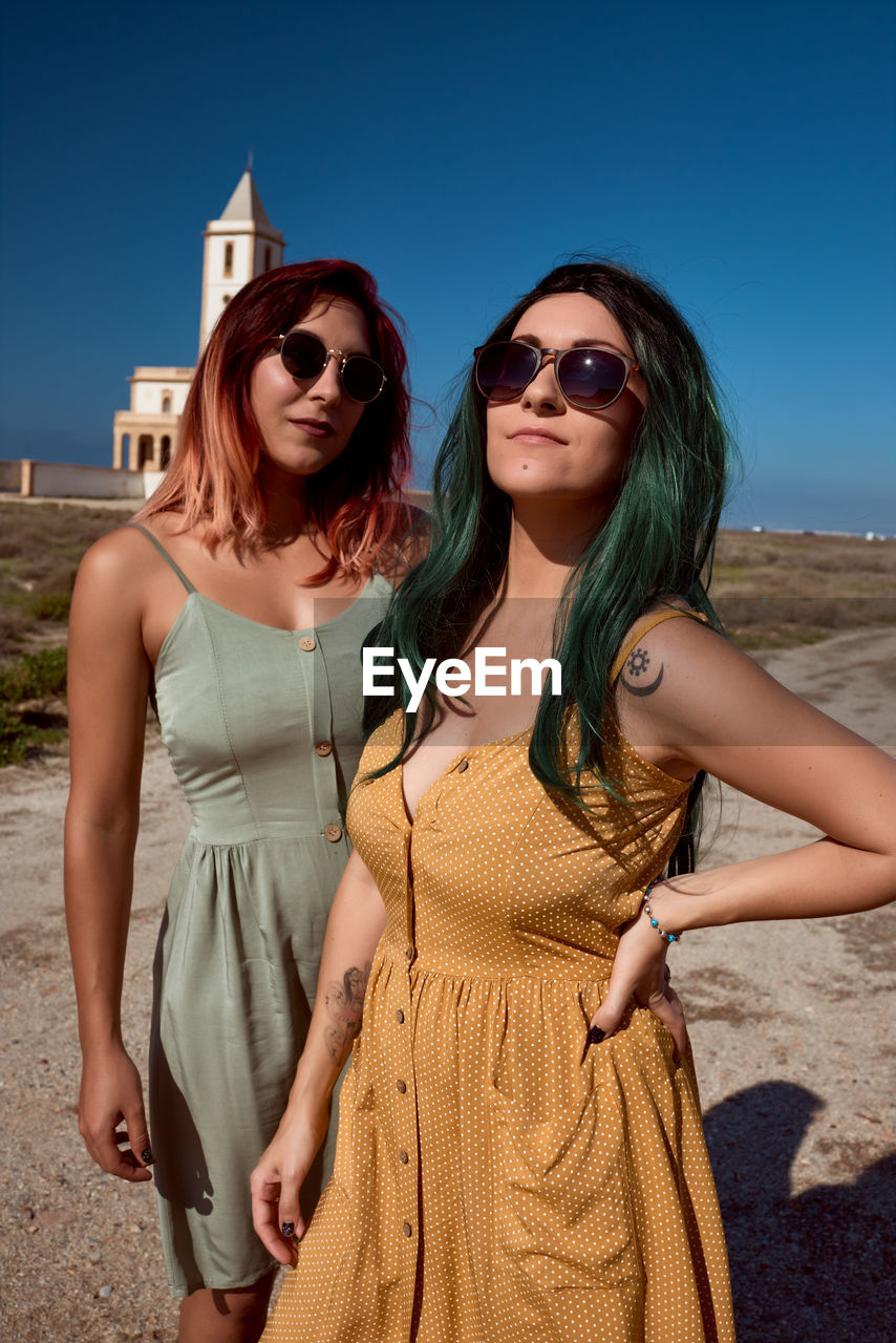 Two young women are posing in dresses in the desert with a church in the background. fashion concept