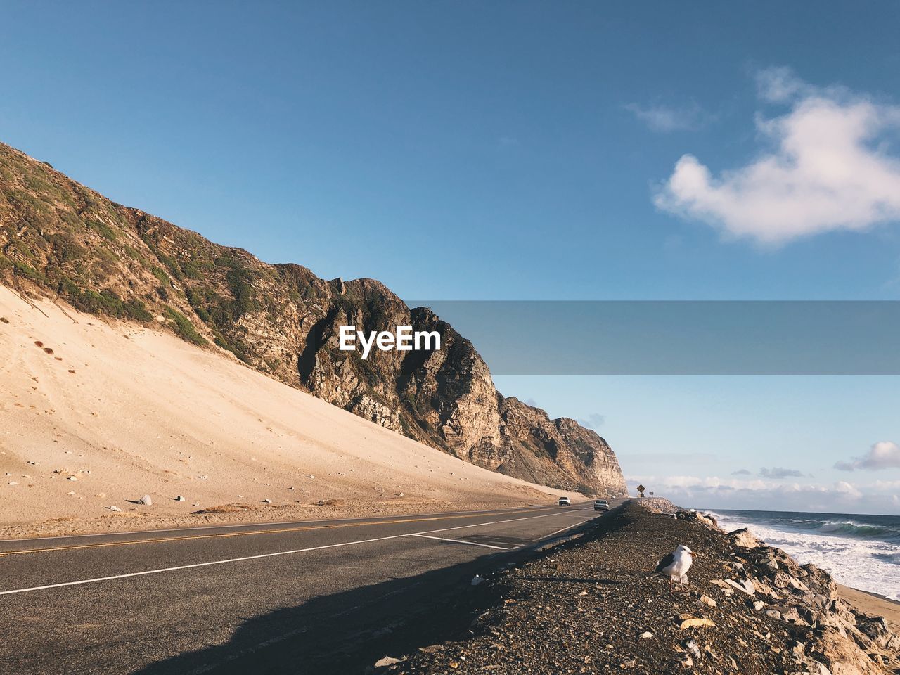 Scenic view of road by sea against blue sky