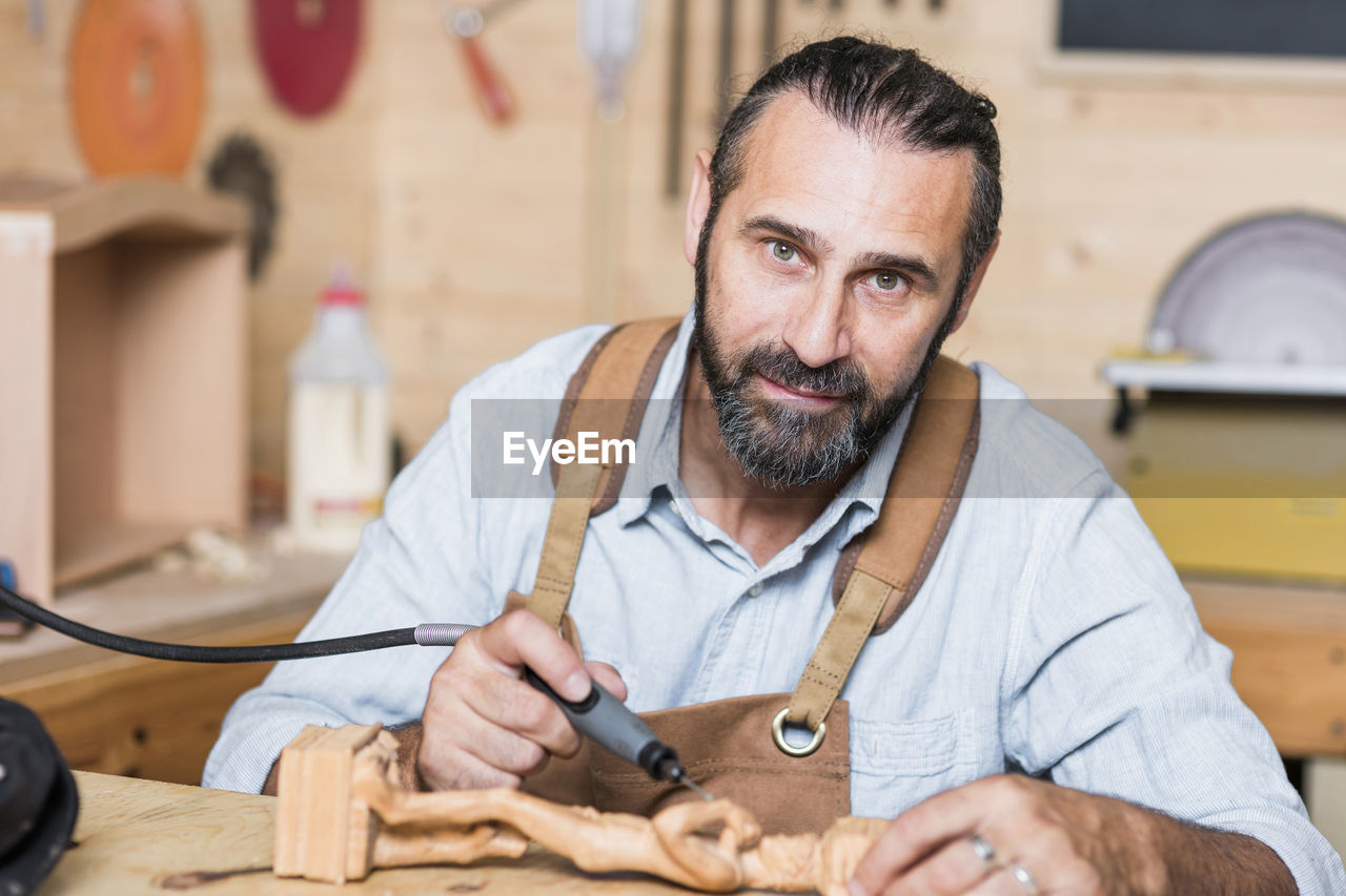 Portrait of carpenter carving on figurine in workshop