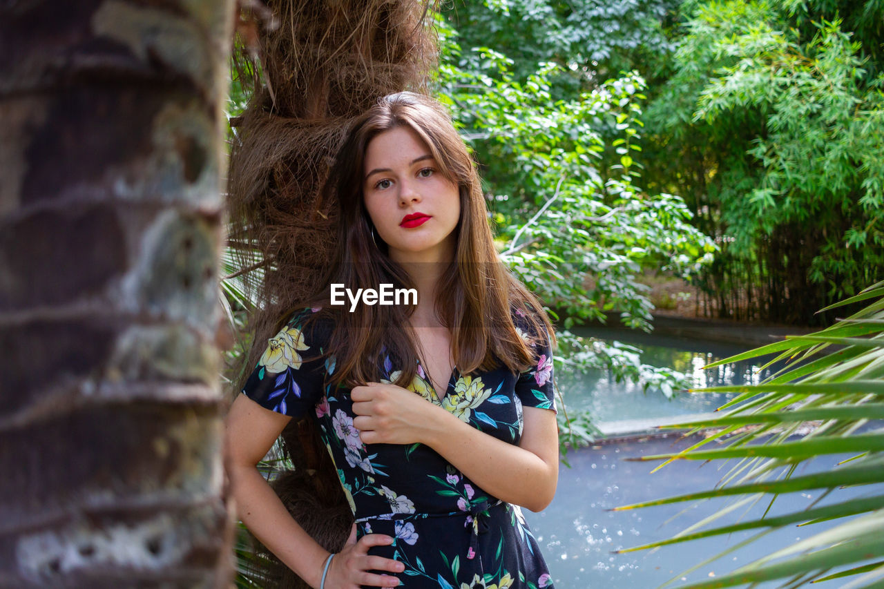 Portrait of beautiful woman standing by tree trunk