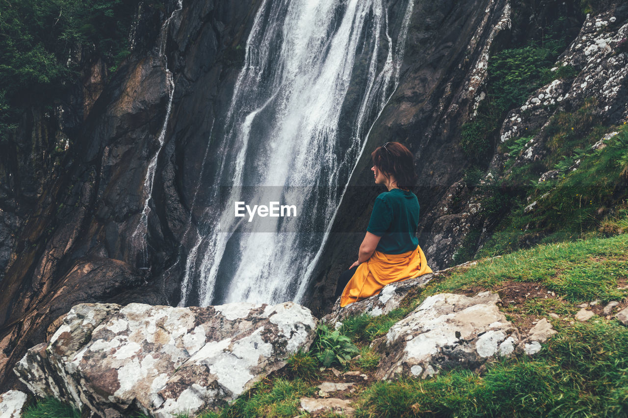 REAR VIEW OF WOMAN SITTING ON ROCK