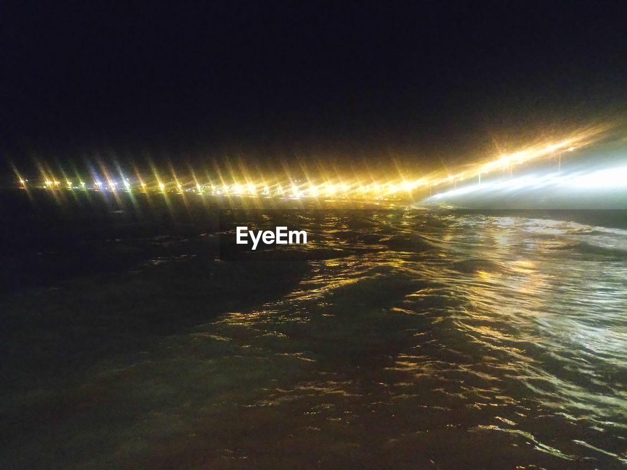 ILLUMINATED STREET BY SEA AGAINST SKY