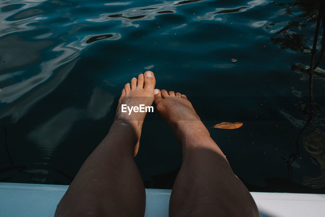 Low section of woman relaxing on pier against lake