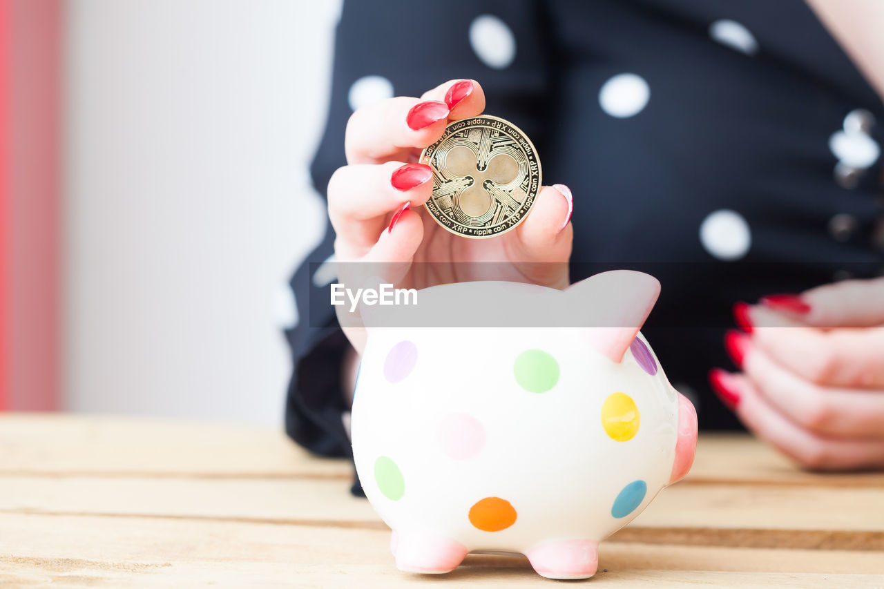 Midsection of woman holding coin over piggy bank at table