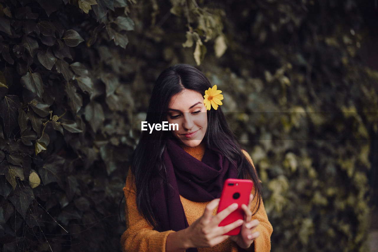 Woman taking a selfie with her phone with flower in her hair