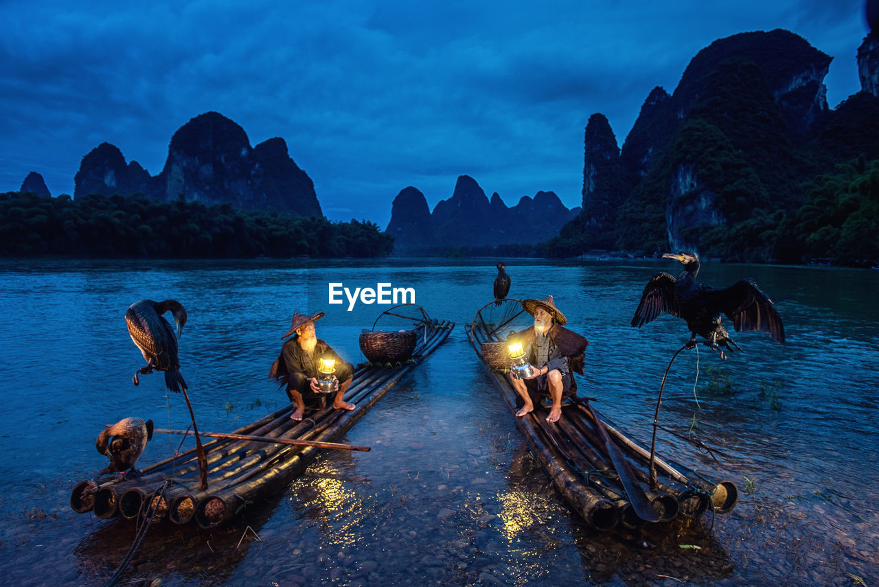 Men with illuminated lanterns sitting on wooden raft in lake