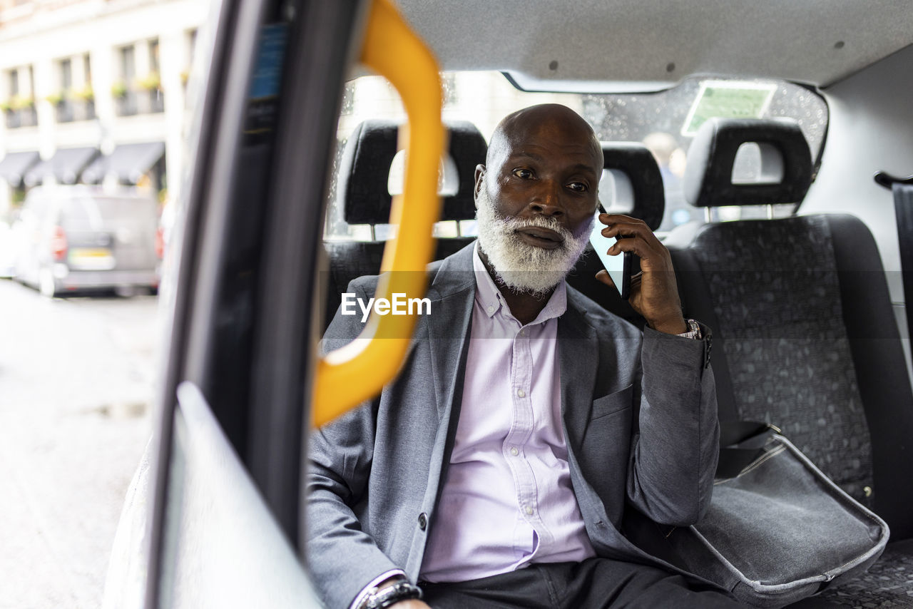 Senior bearded passenger talking on mobile phone in taxi