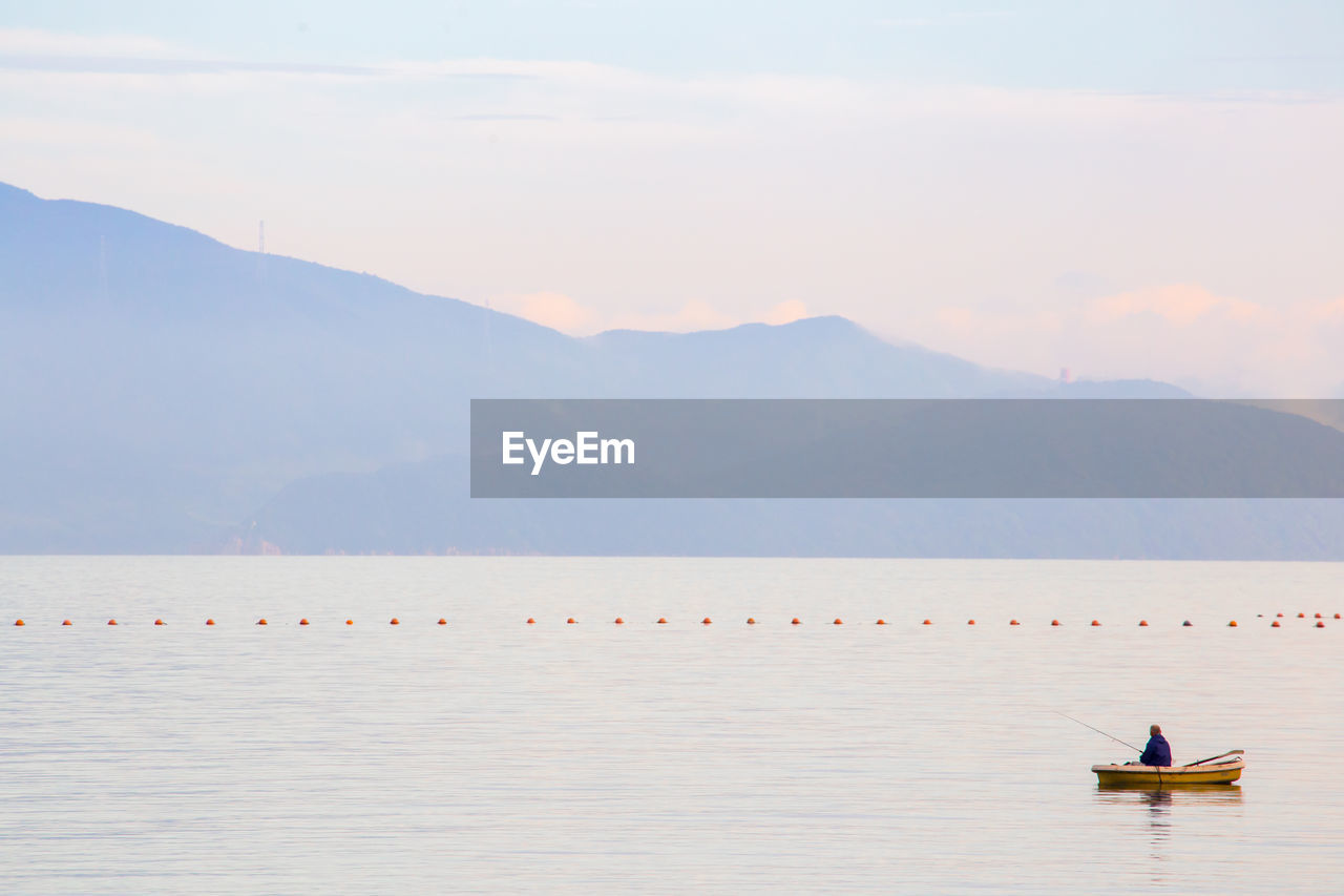 Man fishing in sea while sitting on boat against sky