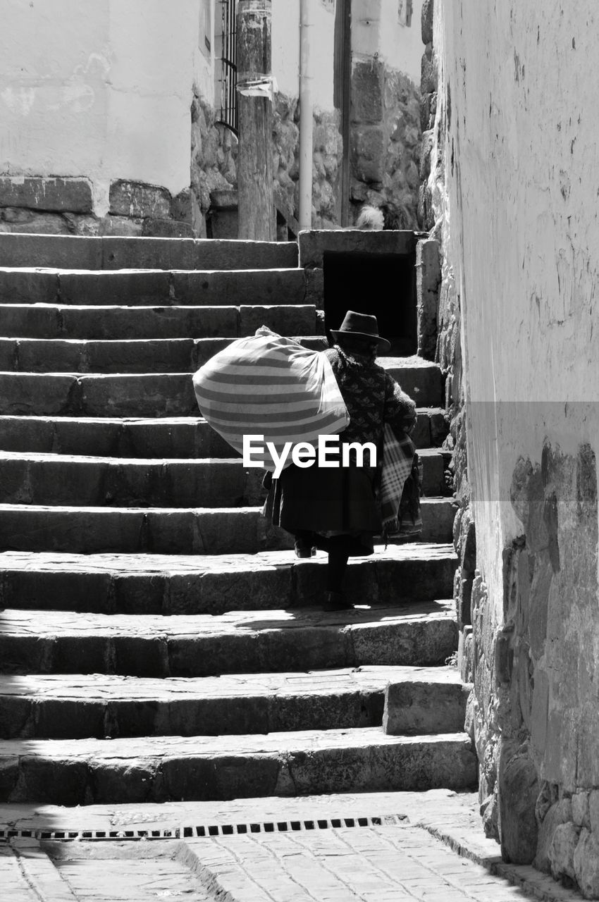 Rear view of senior woman carrying burden while moving up on steps