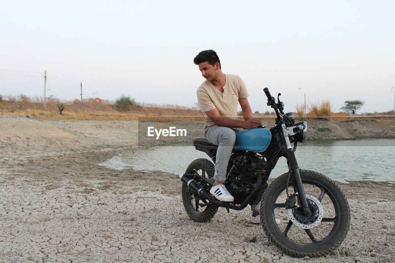 Young man sitting on motorcycle at lakeshore