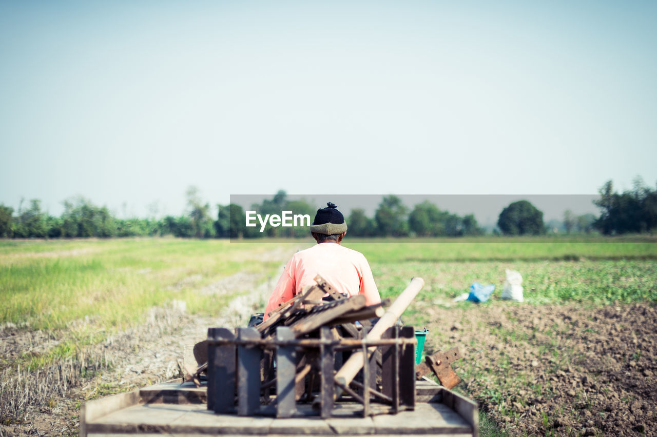 Rear view of man carrying scrap metal on cart through field against clear sky