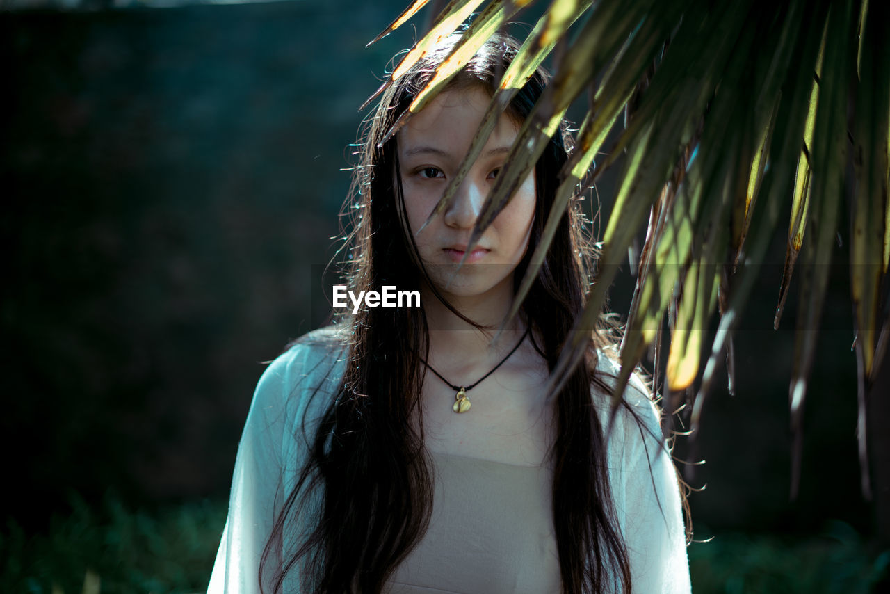 Portrait of young woman standing by plants