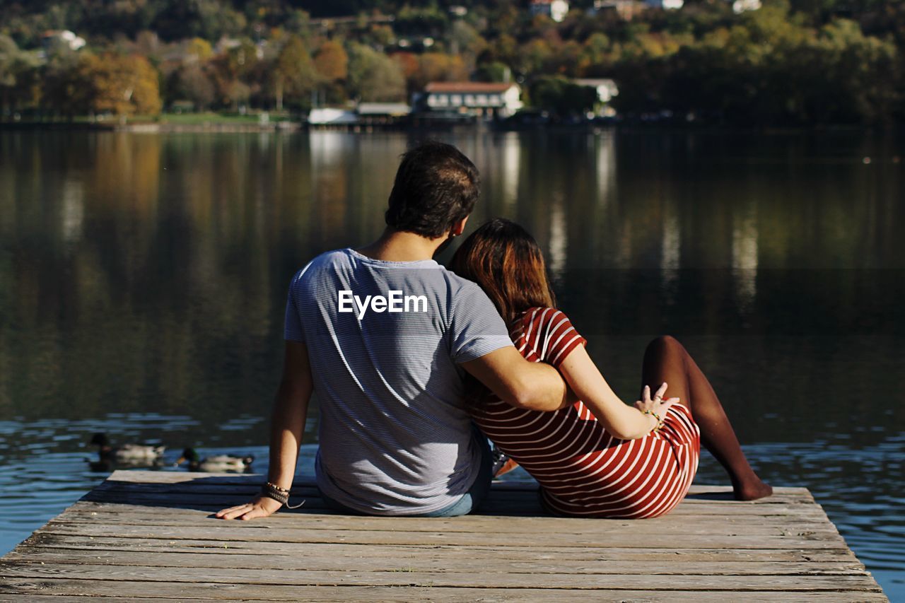 Rear view of couple sitting on pier over lake