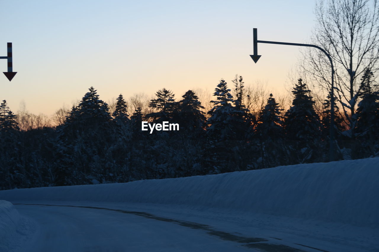 Trees on snow covered field against sky during sunset