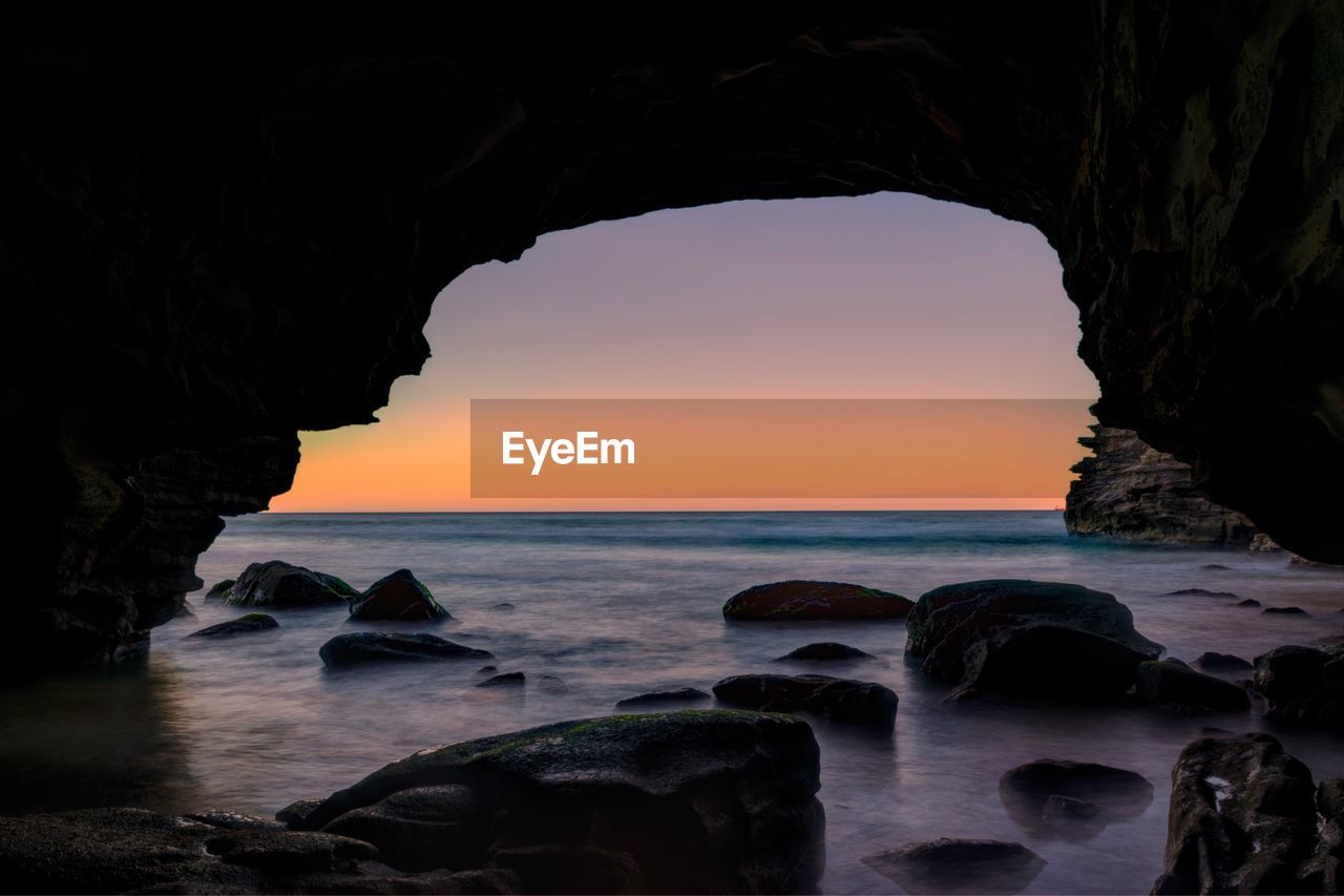 Scenic view of sea seen from cave against sky during sunset