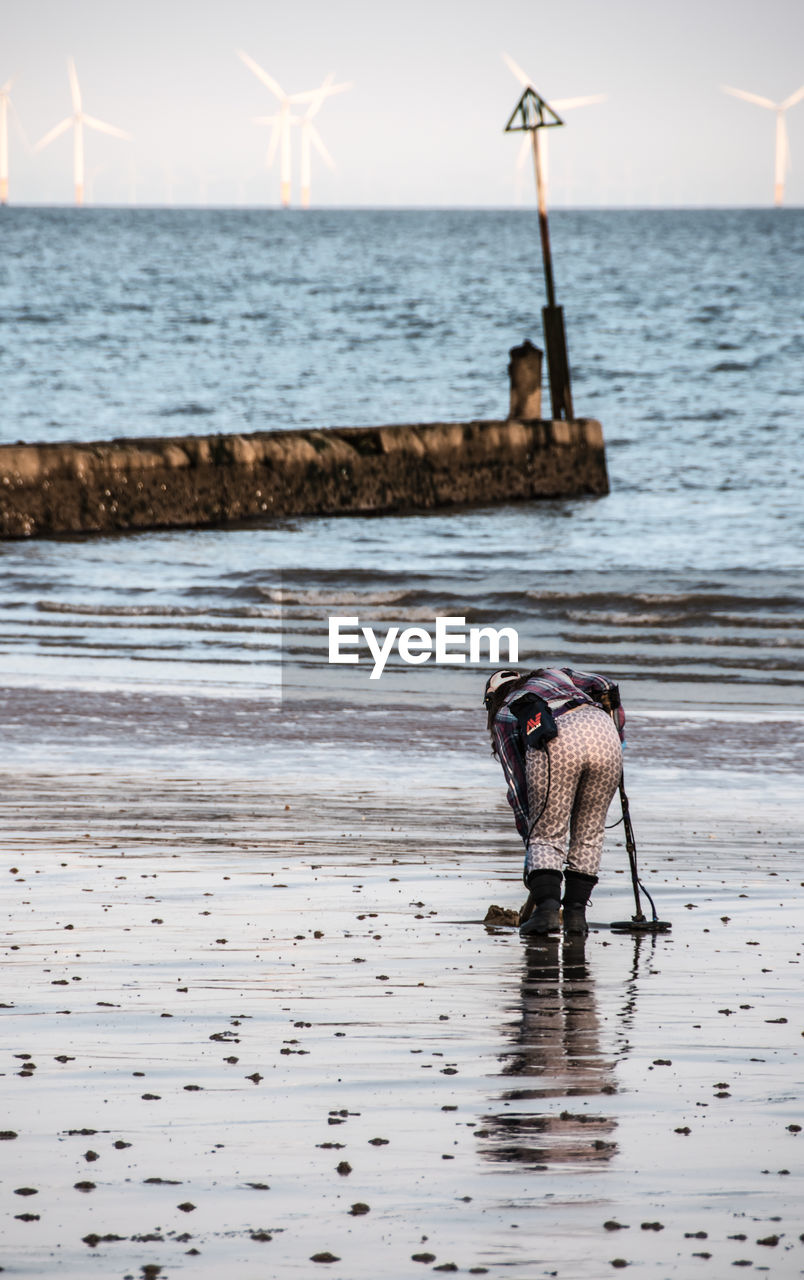 Rear view full length of woman with metal detector at beach