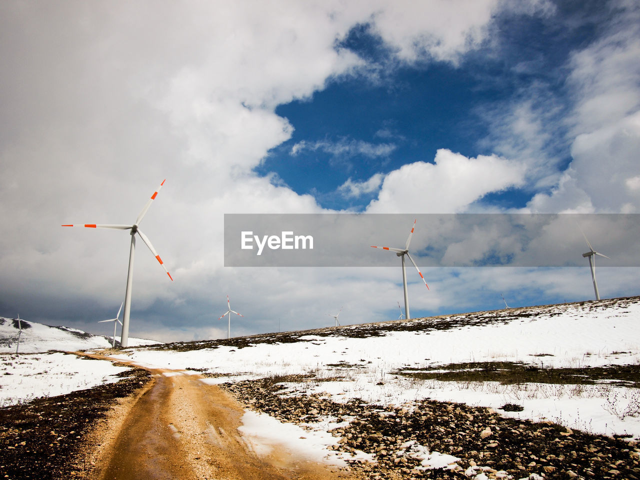 Wind turbines on snowy field against cloudy sky