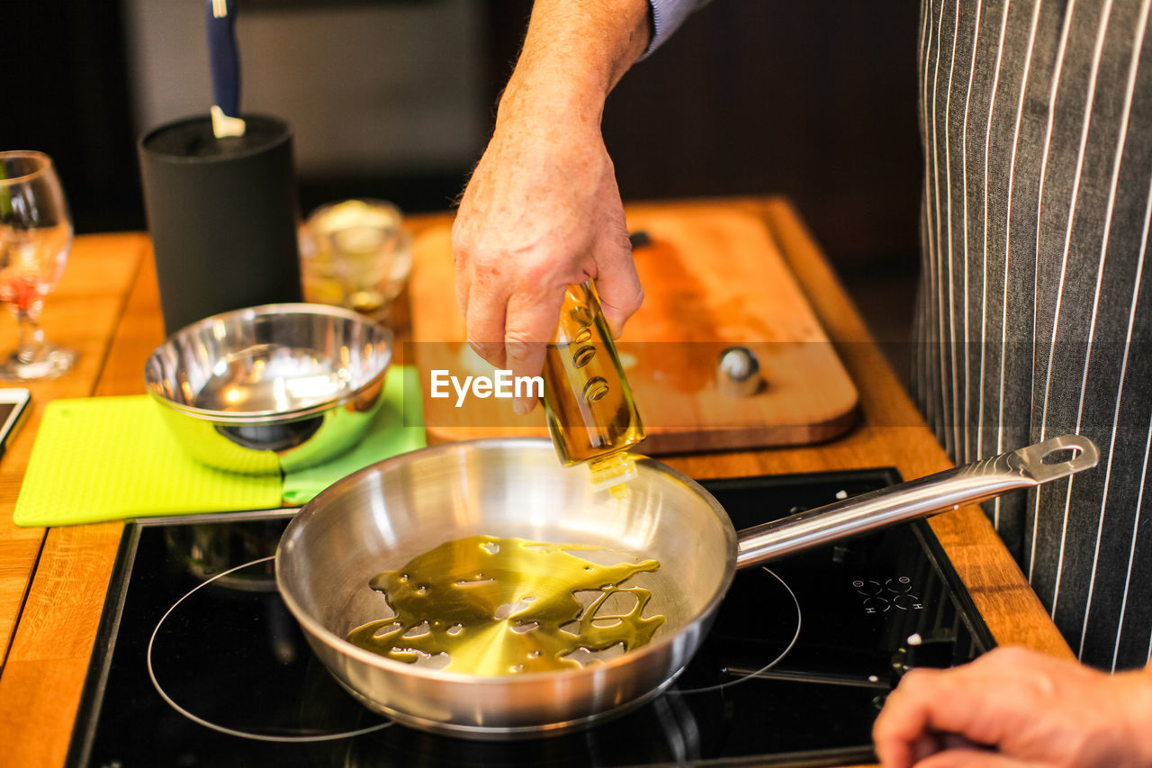 Midsection of man pouring oil in pan while cooking