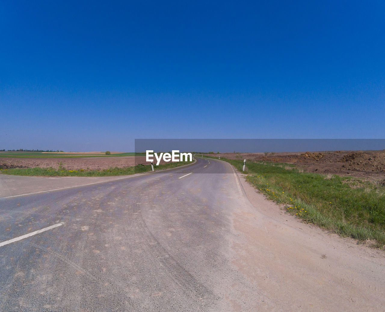 Empty road amidst field against clear blue sky