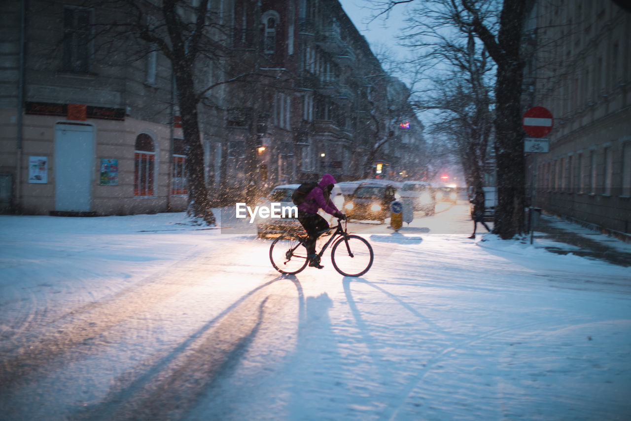 MAN CYCLING ON SNOW COVERED CITY