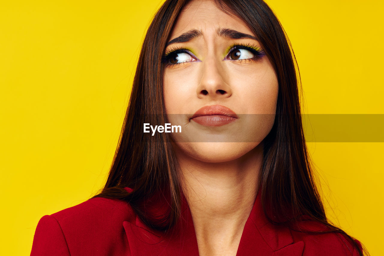 Young woman looking away against yellow background