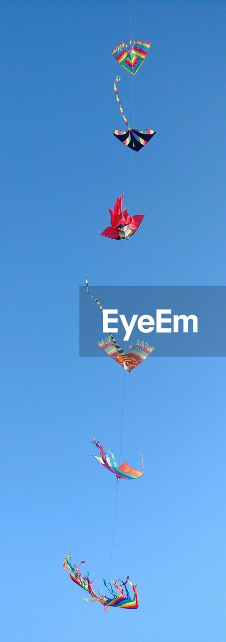 Low angle view of kites flying against clear blue sky