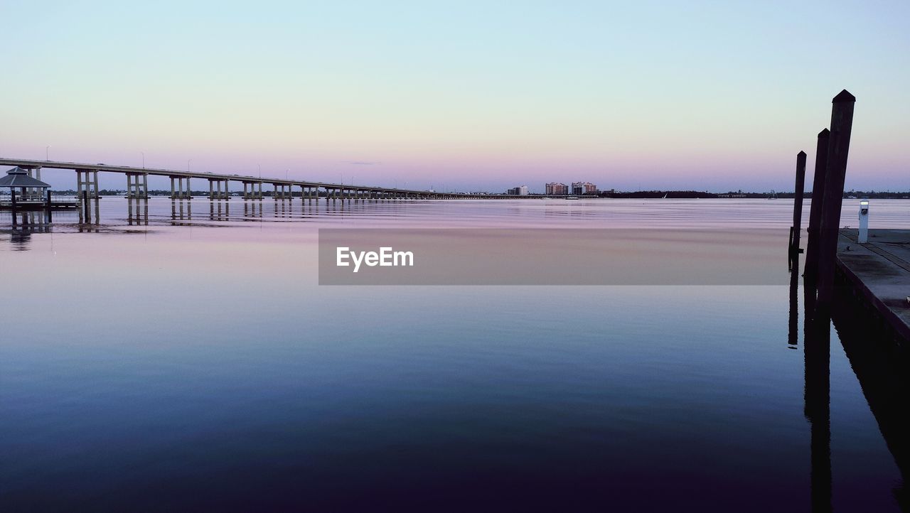 water, sky, reflection, scenics - nature, sea, beauty in nature, tranquility, dawn, nature, sunrise, horizon, tranquil scene, architecture, morning, built structure, ocean, clear sky, no people, bridge, travel destinations, pier, twilight, idyllic, landscape, blue, copy space, environment, bay, outdoors, travel, transportation, coast, shore, tourism, non-urban scene, land, wave, beach, dock, horizon over water