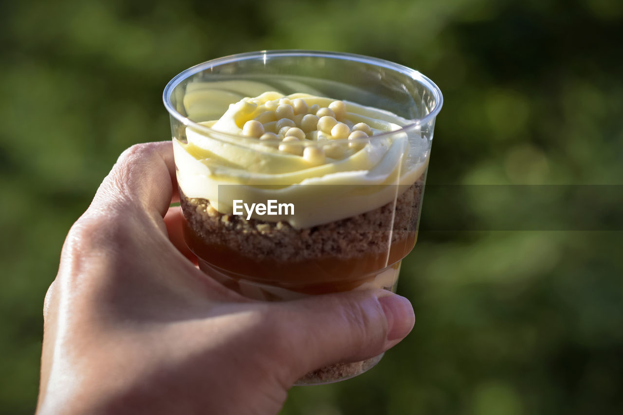 Sweet dessert trifle in transparent glass in woman's hand against green background. copy space.