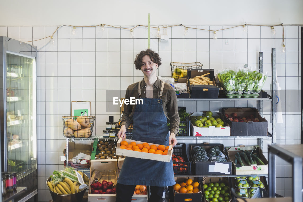 Portrait of smiling male owner with fruit box in store