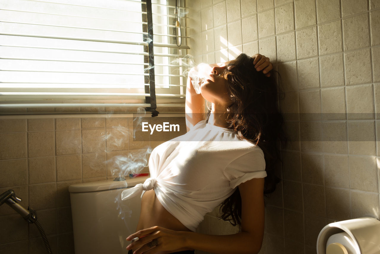 Young woman smoking cigarette in bathroom